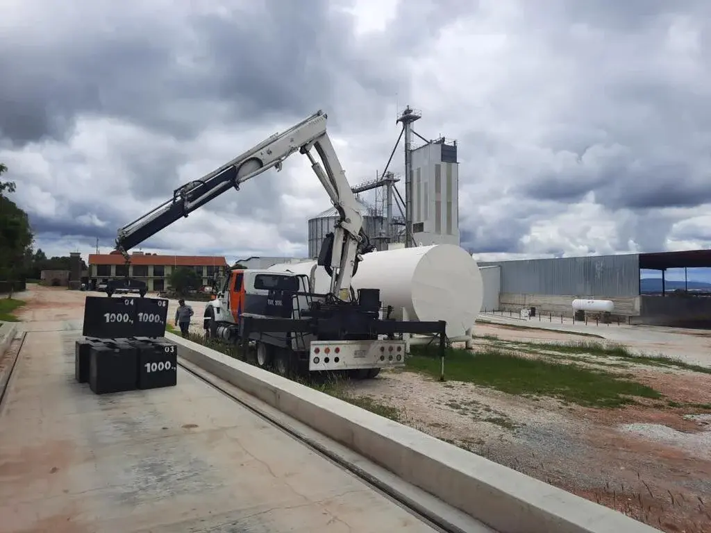 Camión grúa y cargas patrón junto a una báscula camionera en instalaciones industriales